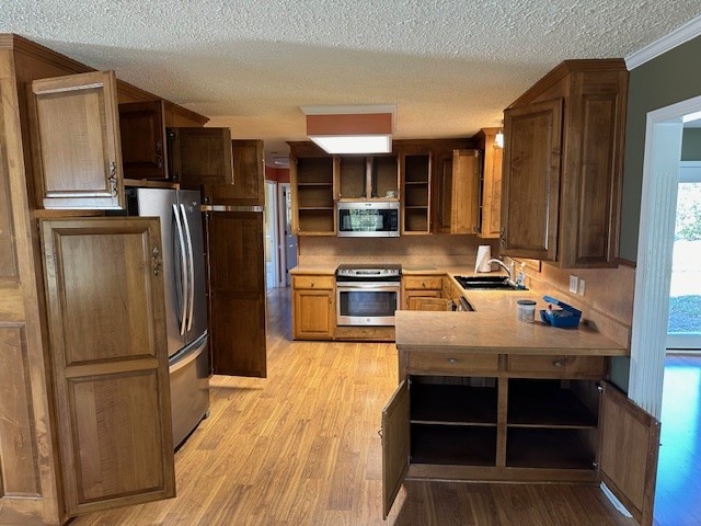 kitchen featuring kitchen peninsula, appliances with stainless steel finishes, light wood-type flooring, crown molding, and sink