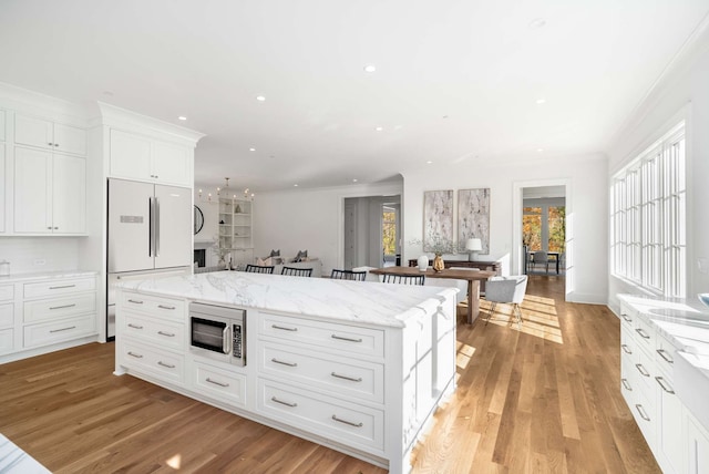 kitchen featuring light wood-type flooring, light stone counters, built in appliances, white cabinets, and a center island