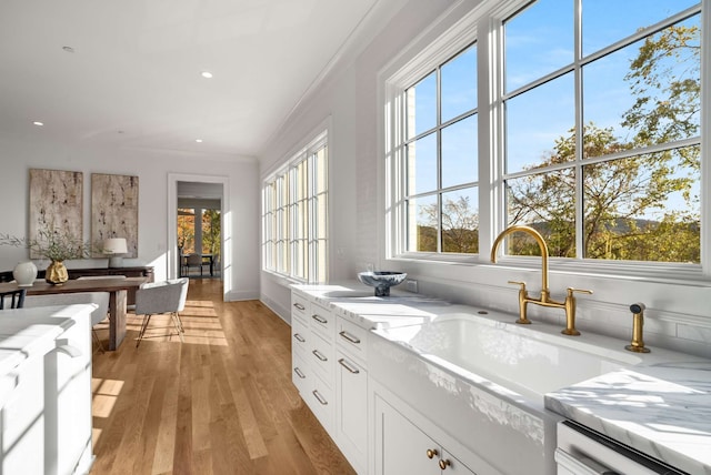 kitchen with white cabinets, light stone countertops, ornamental molding, dishwashing machine, and light hardwood / wood-style floors