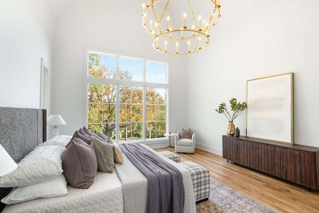 bedroom with multiple windows, light hardwood / wood-style flooring, a high ceiling, and a notable chandelier