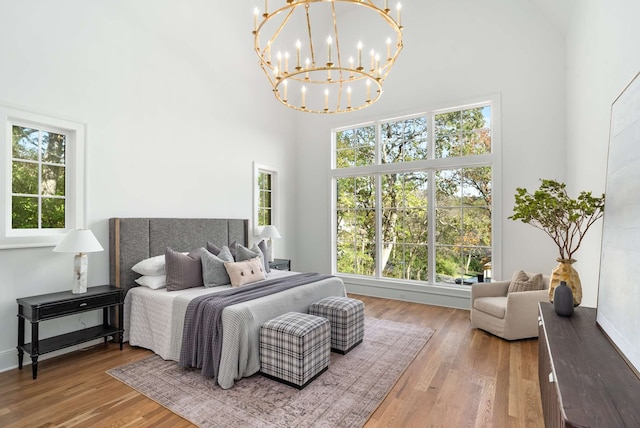 bedroom with a chandelier, a towering ceiling, and wood-type flooring