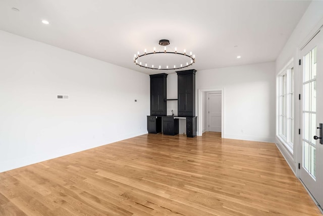 unfurnished living room featuring sink, a chandelier, and light wood-type flooring