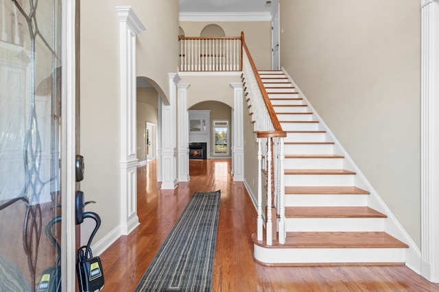 foyer with ornate columns, crown molding, a towering ceiling, and dark hardwood / wood-style flooring