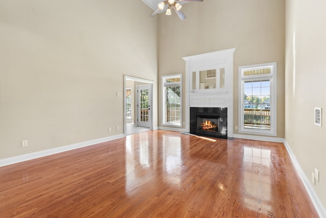 unfurnished living room with ceiling fan, a towering ceiling, and light hardwood / wood-style flooring