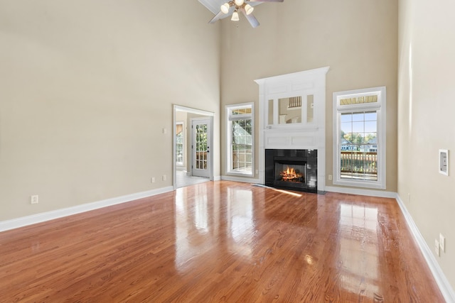 306 Gray Hawk Trl, Clarksville, TN 37043 - unfurnished living room with light wood-style floors, a glass covered fireplace, a ceiling fan, baseboards, and a towering ceiling