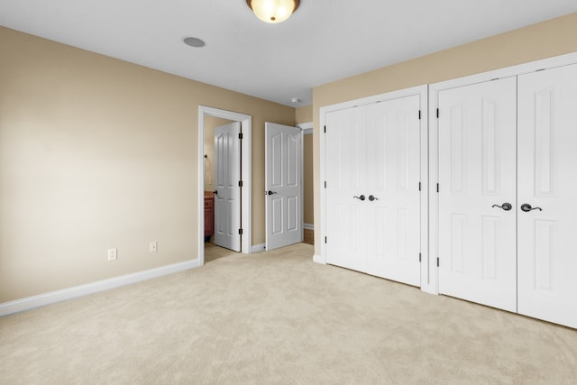 unfurnished bedroom featuring light carpet, multiple closets, and ensuite bath