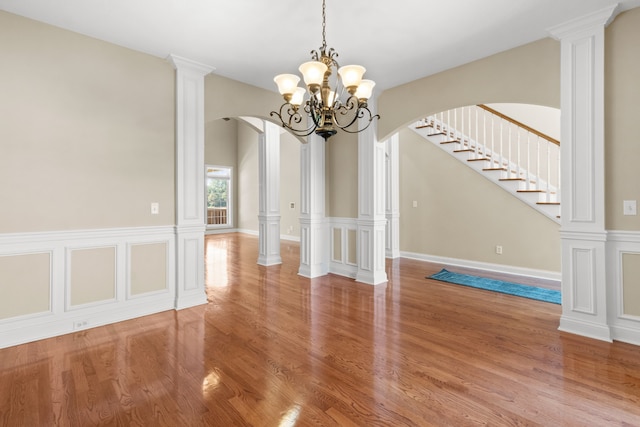 unfurnished dining area with decorative columns, an inviting chandelier, and hardwood / wood-style floors