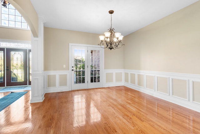 unfurnished dining area featuring french doors, light hardwood / wood-style flooring, and a chandelier