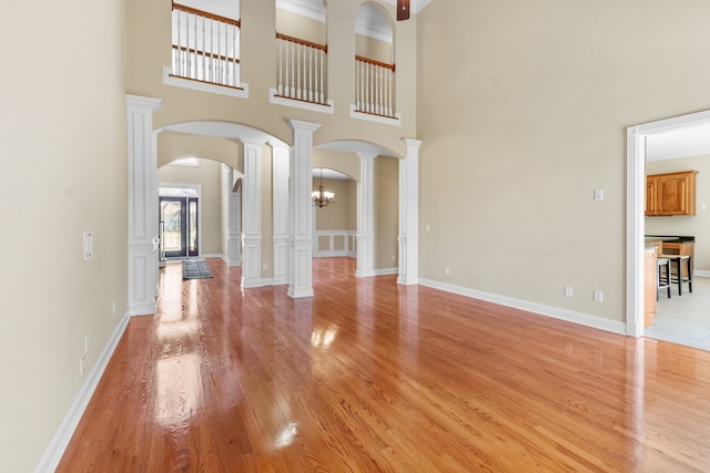 unfurnished living room with an inviting chandelier, light hardwood / wood-style flooring, and a high ceiling