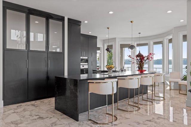 kitchen featuring a water view, dark stone countertops, pendant lighting, and an island with sink