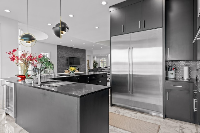 kitchen featuring decorative backsplash, wine cooler, a kitchen island with sink, built in fridge, and sink