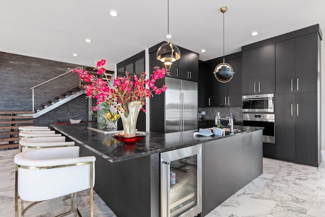 kitchen featuring a kitchen island with sink, stainless steel appliances, backsplash, wine cooler, and pendant lighting