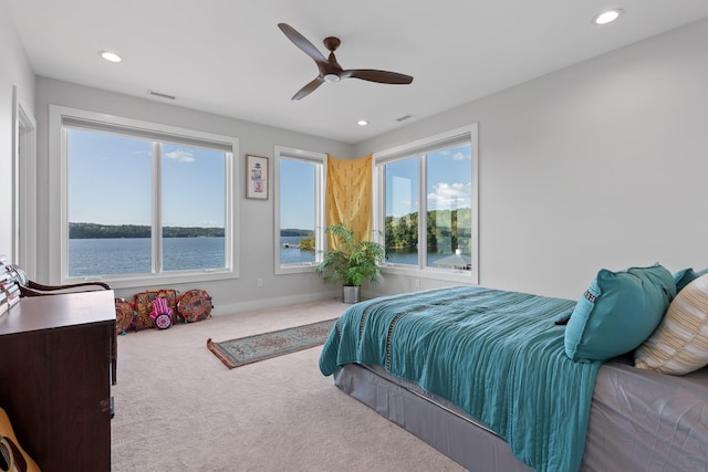 bedroom with light colored carpet, a water view, and ceiling fan