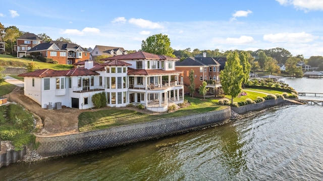 rear view of house featuring a balcony, a water view, and a lawn