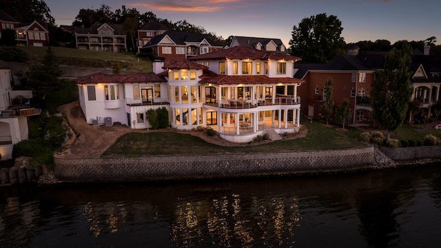 back house at dusk featuring a yard, a water view, and a balcony