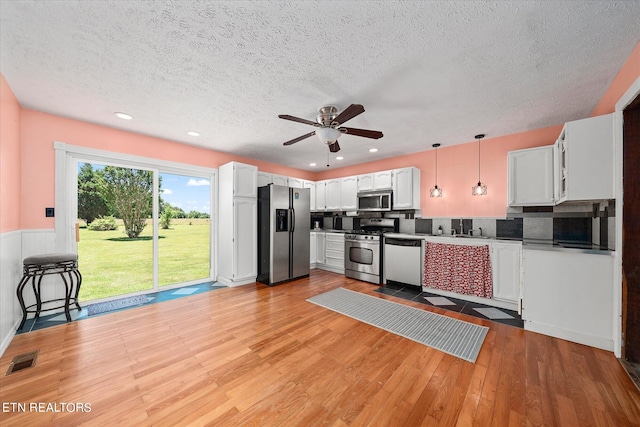 kitchen with appliances with stainless steel finishes, backsplash, hanging light fixtures, white cabinets, and light hardwood / wood-style flooring