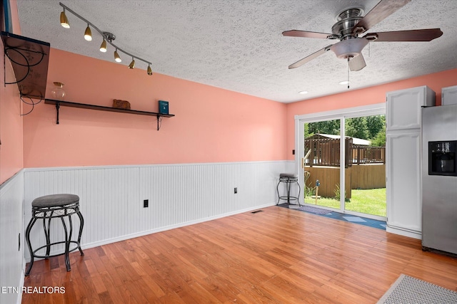 unfurnished room with a textured ceiling, ceiling fan, wainscoting, and wood finished floors