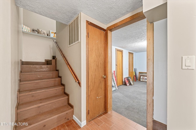 stairway featuring a textured ceiling and carpet