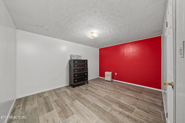 empty room with a textured ceiling, wood finished floors, and baseboards