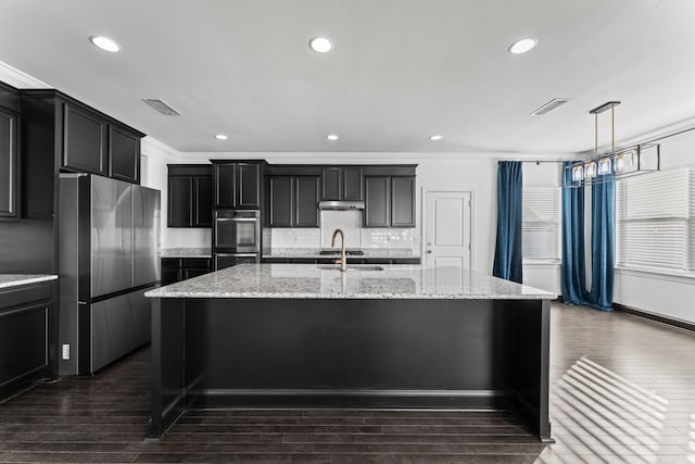 kitchen with light stone counters, an island with sink, dark wood-type flooring, crown molding, and stainless steel appliances