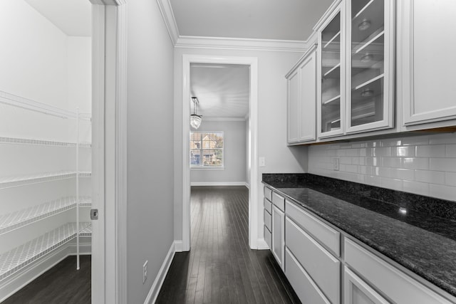 bar featuring backsplash, dark stone counters, crown molding, white cabinetry, and dark hardwood / wood-style flooring