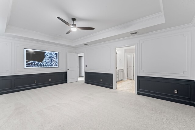 unfurnished bedroom featuring ensuite bath, a raised ceiling, ceiling fan, light carpet, and ornamental molding