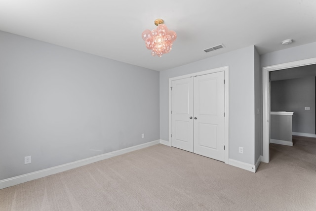 unfurnished bedroom featuring a closet, light carpet, and a notable chandelier