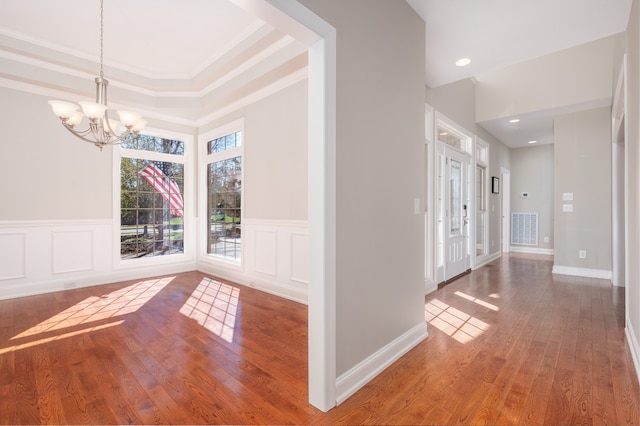 foyer featuring ornamental molding, a chandelier, wood-type flooring, and a raised ceiling