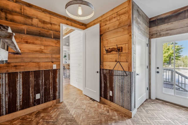 entryway with light parquet floors and wood walls