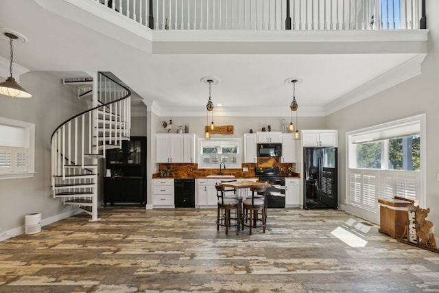 kitchen with hanging light fixtures, wood-type flooring, black appliances, white cabinets, and a towering ceiling