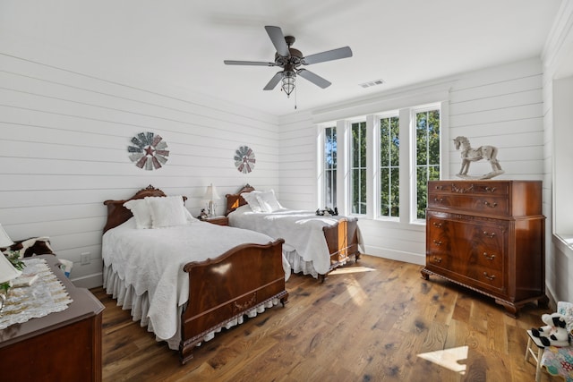 bedroom featuring wooden walls, wood-type flooring, and ceiling fan