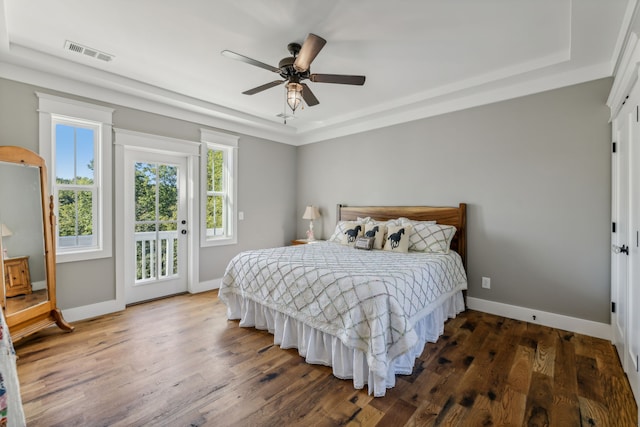 bedroom with dark wood-type flooring, ceiling fan, a tray ceiling, and access to exterior