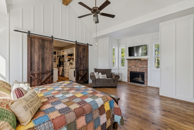 bedroom featuring a spacious closet, a barn door, a brick fireplace, dark hardwood / wood-style flooring, and ceiling fan