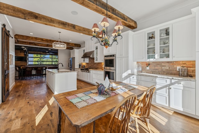 kitchen with an island with sink, white cabinetry, stainless steel appliances, pendant lighting, and exhaust hood