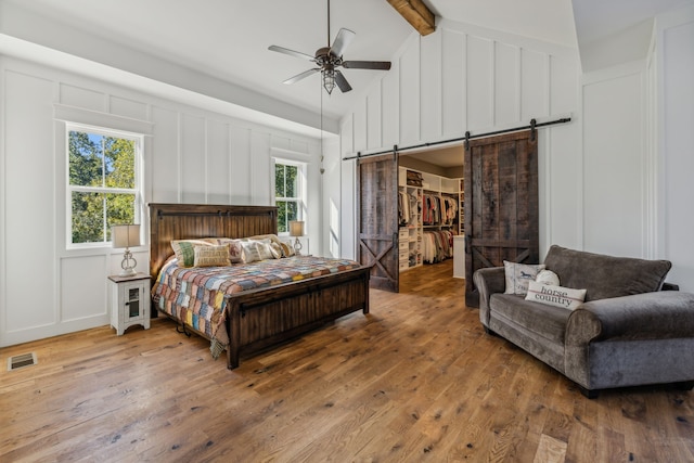 bedroom featuring a spacious closet, wood-type flooring, multiple windows, and a barn door