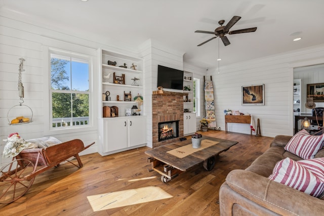 living room featuring wooden walls, wood-type flooring, built in features, a fireplace, and ceiling fan