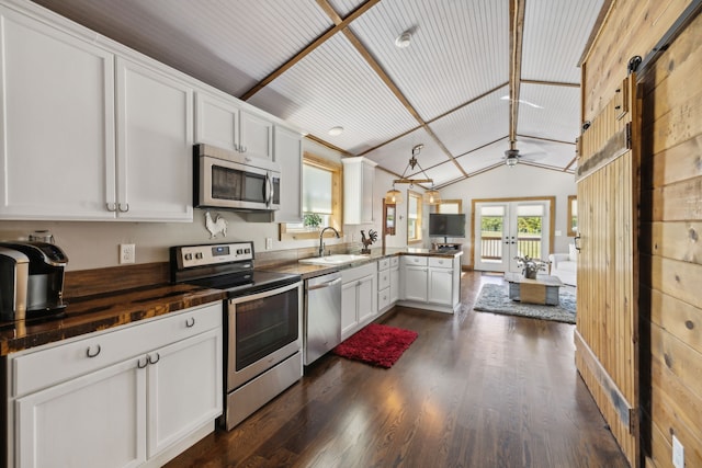 kitchen featuring a barn door, kitchen peninsula, stainless steel appliances, vaulted ceiling, and white cabinets