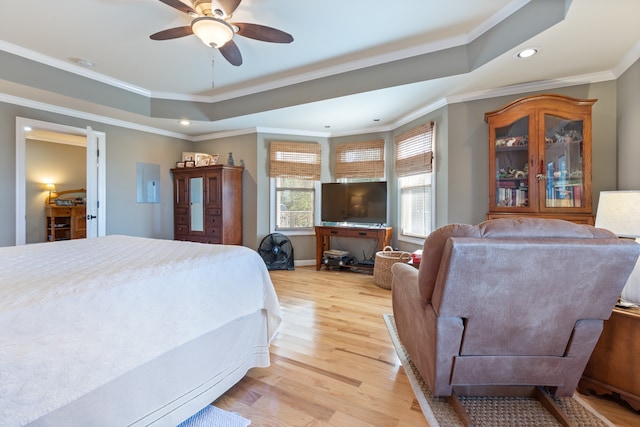 bedroom with ceiling fan, ornamental molding, a tray ceiling, and light wood-type flooring