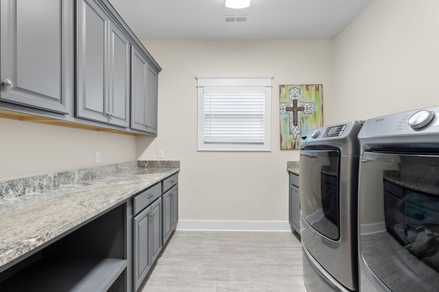 washroom with light hardwood / wood-style flooring, washer and dryer, and cabinets