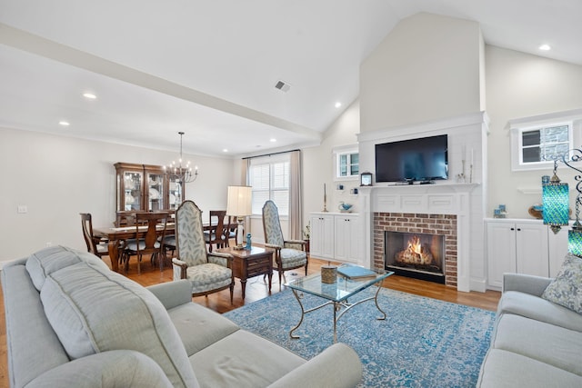 living room featuring an inviting chandelier, light hardwood / wood-style flooring, high vaulted ceiling, and a brick fireplace