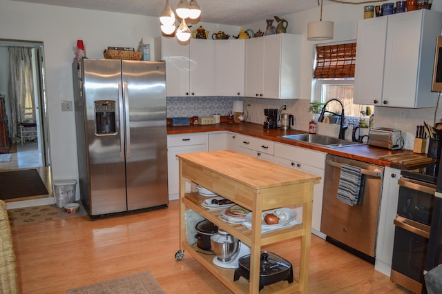 kitchen with appliances with stainless steel finishes, sink, light wood-type flooring, pendant lighting, and white cabinets