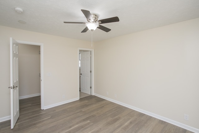 unfurnished bedroom featuring a spacious closet, hardwood / wood-style floors, a textured ceiling, and ceiling fan