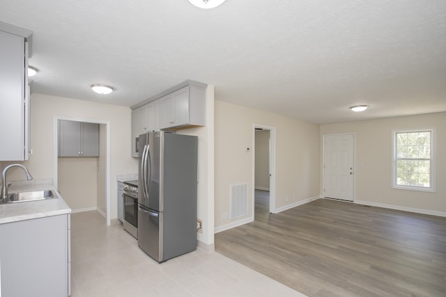 kitchen featuring gray cabinetry, sink, appliances with stainless steel finishes, a textured ceiling, and light hardwood / wood-style floors