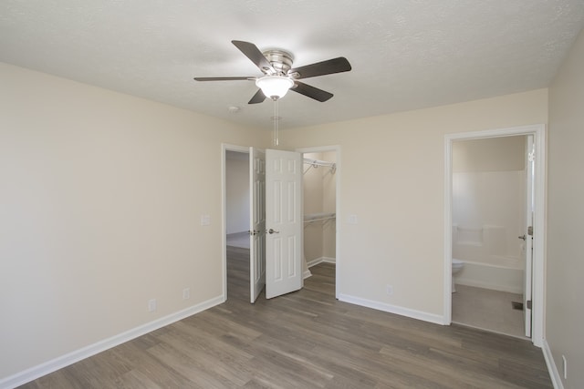 unfurnished bedroom with a spacious closet, wood-type flooring, connected bathroom, and ceiling fan