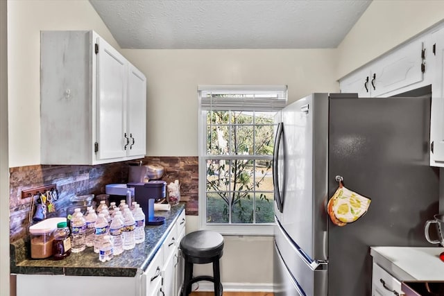 kitchen with white cabinetry, tasteful backsplash, a textured ceiling, and stainless steel refrigerator