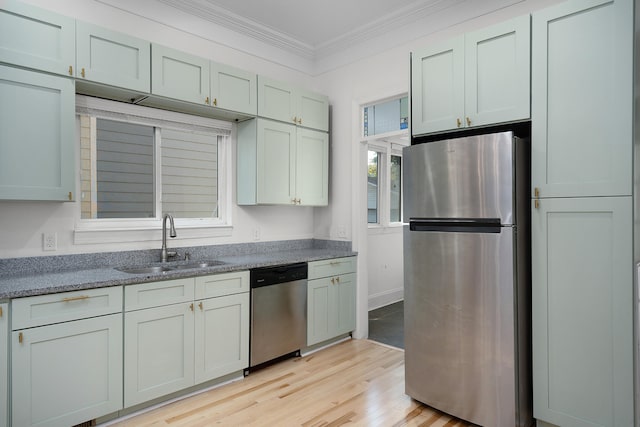 kitchen with dark stone countertops, sink, crown molding, appliances with stainless steel finishes, and light hardwood / wood-style floors