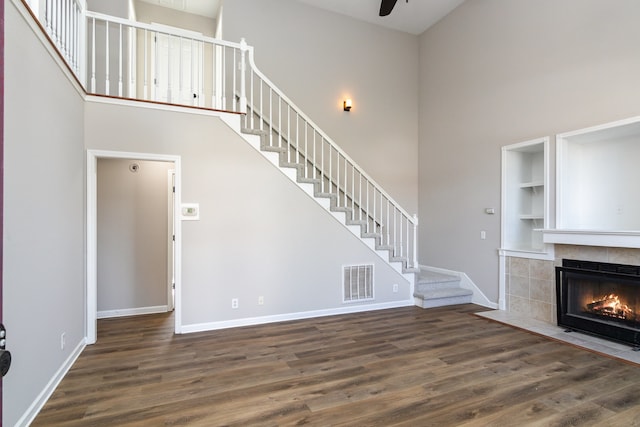 unfurnished living room featuring a tiled fireplace, a towering ceiling, and dark hardwood / wood-style flooring