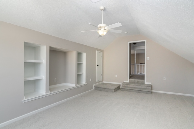 interior space featuring carpet, vaulted ceiling, a textured ceiling, built in shelves, and ceiling fan