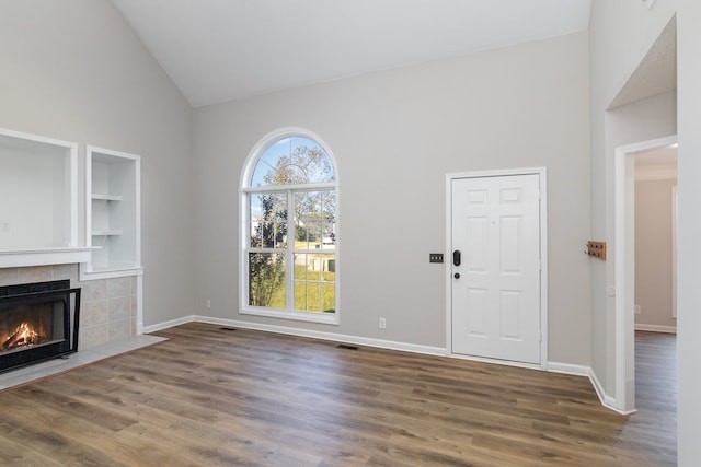 unfurnished living room with built in shelves, dark wood-type flooring, a fireplace, and high vaulted ceiling