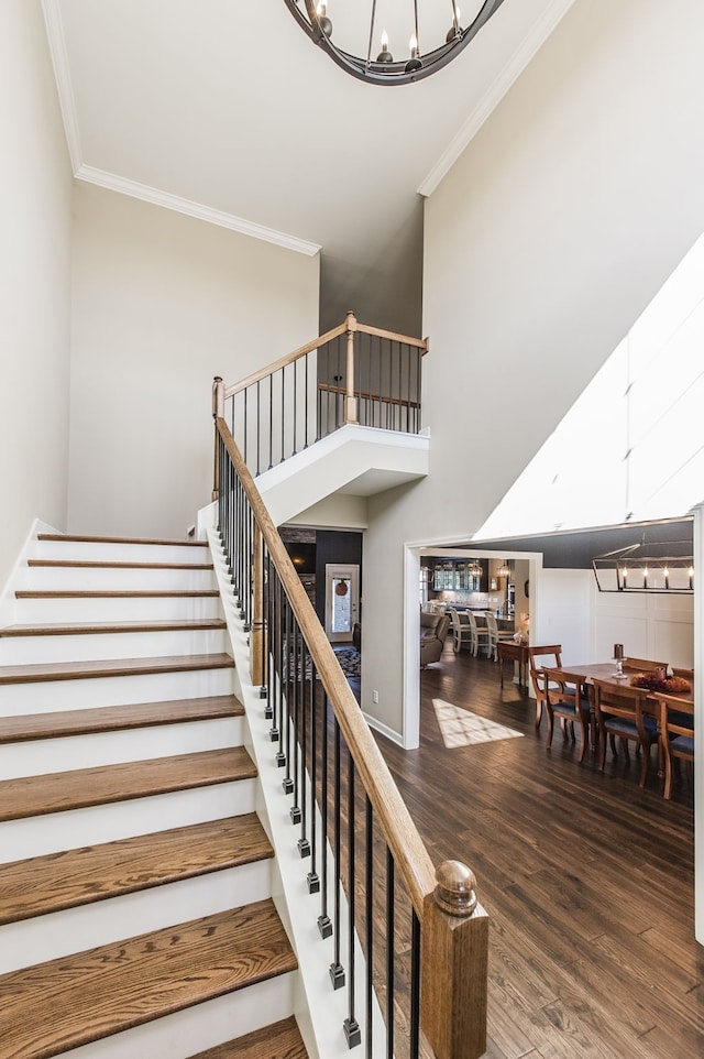 staircase featuring crown molding, wood-type flooring, and an inviting chandelier